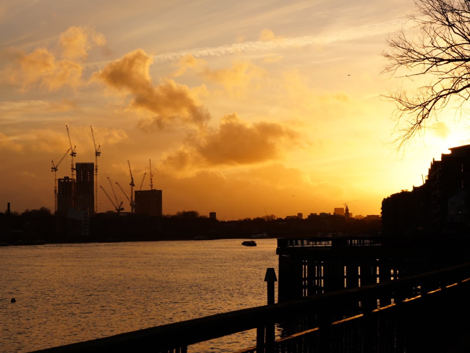 Sunset over the Thames with construction cranes silhouetted against a golden sky